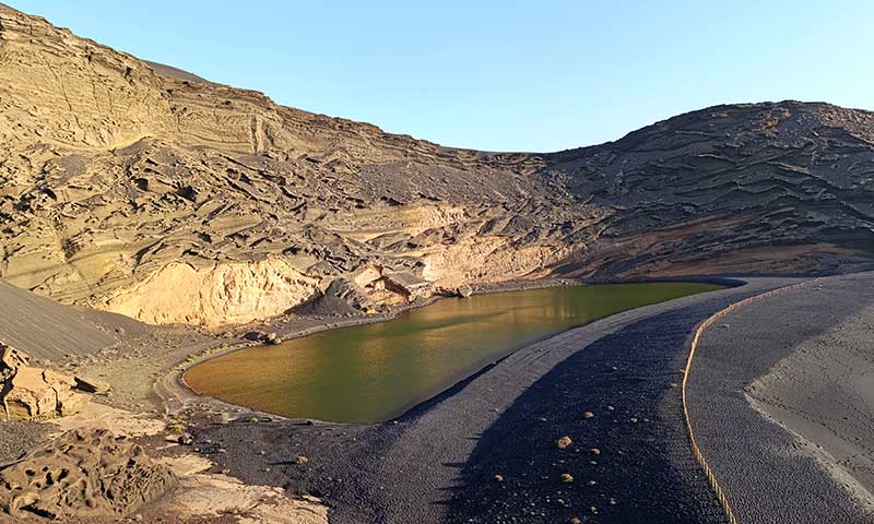 Una fotografía de un lago verde en una playa de arena negra