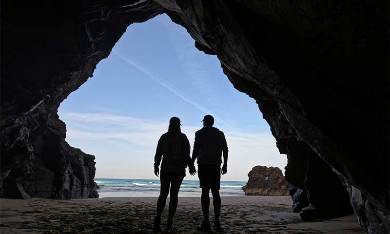 Una fotografía de una pareja caminando de espaldas en una cueva de piedra en una playa