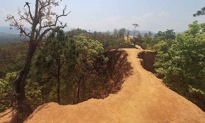 Sendero estrecho de tierra rojiza en la cresta del Cañón de Pai rodeado de árboles y vegetación en Tailandia