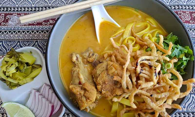 Plato de Khao Soi tradicional tailandés con sopa de curry amarillo fideos crujientes y pollo en Chiang Mai