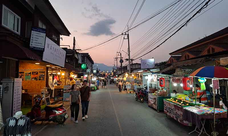 Puestos de comida callejera y personas paseando por el Night Market al atardecer en Tailandia