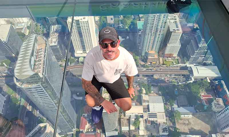 Hombre posando agachado sobre la plataforma de cristal transparente en el mirador Mahanakhon SkyWalk de Bangkok