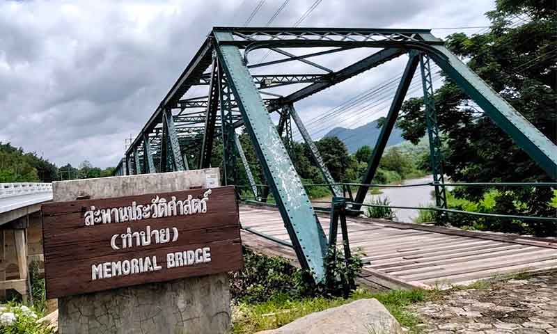 Cartel de madera con el texto Memorial Bridge frente al puente historico de hierro en Tailandia