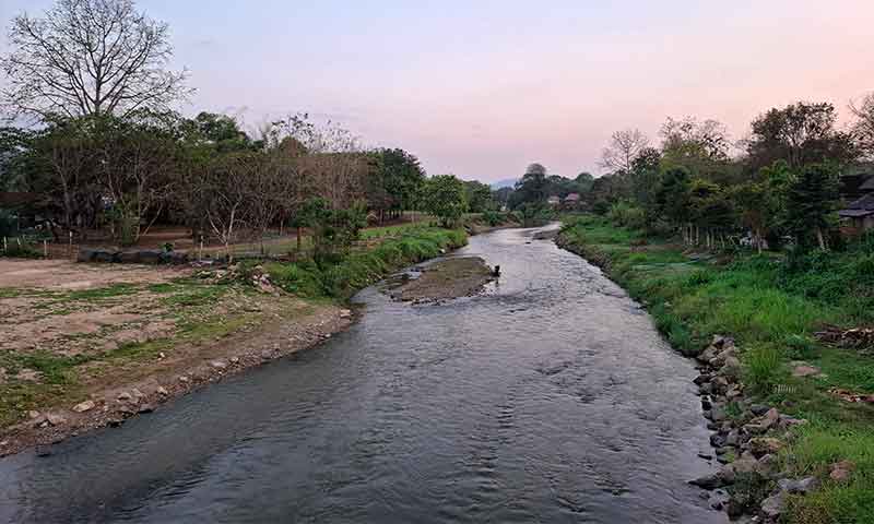 Paisaje tranquilo del río Pai fluyendo entre vegetación y árboles al atardecer en Tailandia
