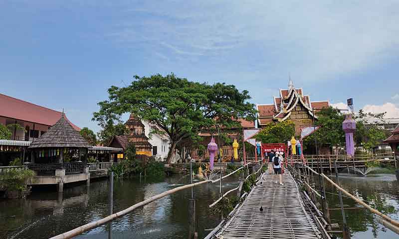 Puente de bambú sobre el estanque con peces en Wat Chet Lin, un tranquilo templo del centro histórico de Chiang Mai.