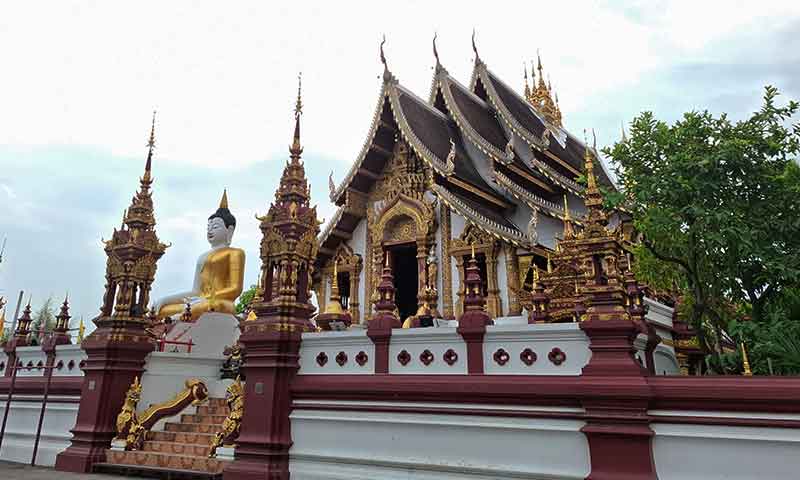 ista exterior de Wat Rajamontean destacando su viharn de colores burdeos y dorados y la gran estatua del Buda blanco sentado en Chiang Mai.