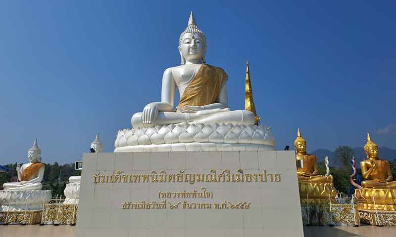 Estatua blanca de Buda sobre base dorada y estatuas adyacentes en el templo de Pai Tailandia
